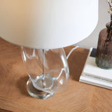 Close-up of the Endon Bramleigh table lamp's clear glass ellipsoid base and white shade on a wooden console beside books and a brown glass vase.