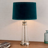 Endon Danehurst table lamp with clear hammered glass base, nickel metalwork and teal velvet tapered shade, lit on a wooden sideboard.