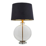 Endon Bramleigh table lamp with a clear glass ellipsoid base, antique brass stem and tapered black faux suede shade, on a white background.