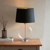 Endon Bramleigh table lamp with clear glass ellipsoid base and black tapered shade with gold interior, on a wooden console beside books and a vase.