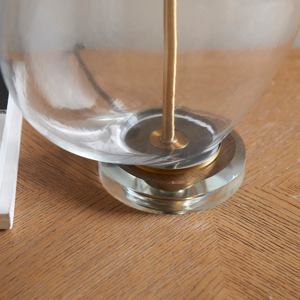 Close-up of the Endon Bramleigh table lamp's clear glass ellipsoid base and antique brass fitting resting on a herringbone wooden floor.