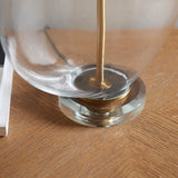 Close-up of the Endon Bramleigh table lamp's clear glass ellipsoid base and antique brass fitting resting on a herringbone wooden floor.