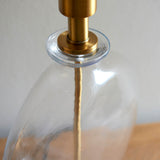 Close-up of the Endon Bramleigh table lamp showing the clear glass ellipsoid base and antique brass neck fitting.