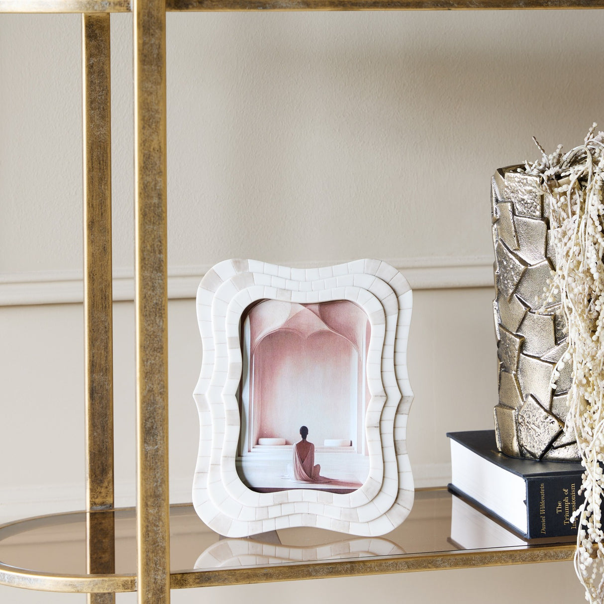 Libra Interiors Mosaic Tiled Resin Photo Frame in ivory with wave-shaped scalloped border, displayed on a mirrored gold shelf beside a book and vase.