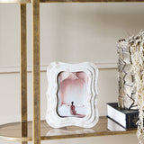 Libra Interiors Mosaic Tiled Resin Photo Frame in ivory with wave-shaped scalloped border, displayed on a mirrored gold shelf beside a book and vase.