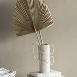 Libra Interiors Arrowhead Fan Palm Leaf artificial stems arranged in a speckled ceramic vase with looped handles, set on stacked books against a neutral wall.