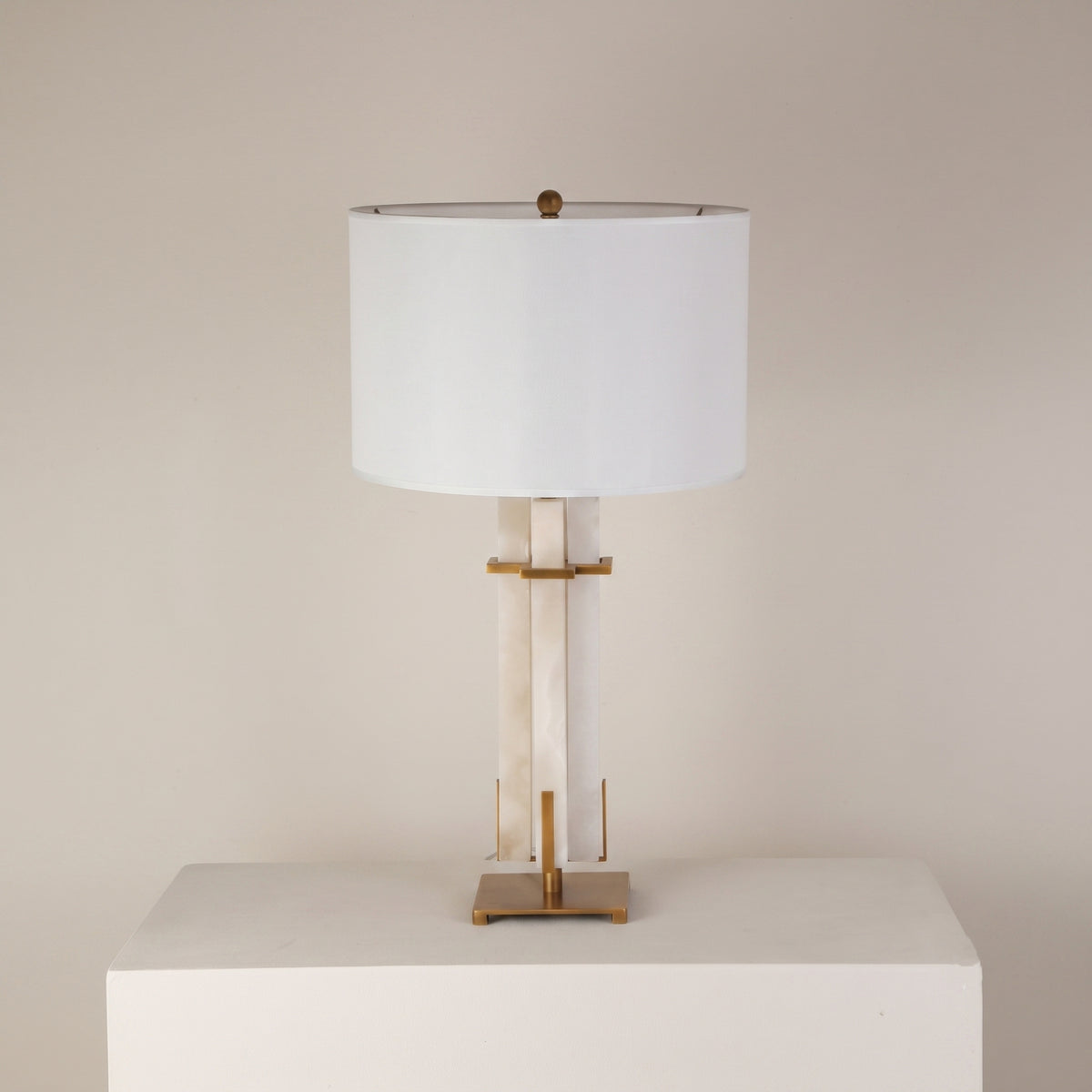 Pilaster table lamp with a vertical alabaster column set in a brushed brass frame, topped with a white fabric drum shade, shown against a plain light background.