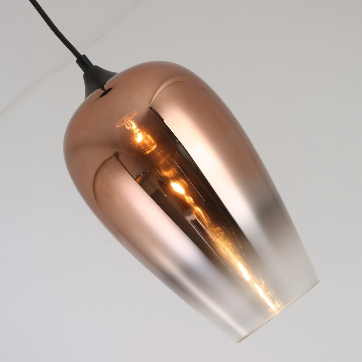 The Slice Glass Pendant Light - Copper showcases a smooth, reflective copper finish with a visible glowing bulb, suspended from a black cord against a plain white background.