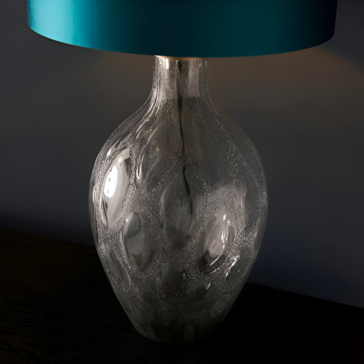 Endon Brenstead table lamp with textured charcoal-tinted artisan glass base and teal satin drum shade on a dark wood surface.