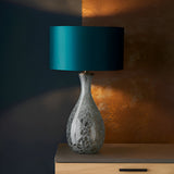 Carldale Table Lamp in Bronze with grey cloud-effect glass hourglass base, brushed bronze fittings, and teal drum shade on a wooden sideboard.