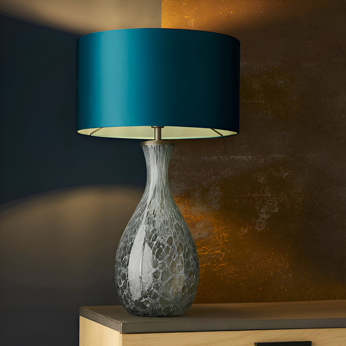 Carldale Table Lamp in bronze, grey cloud-effect glass hourglass base with teal drum shade, shown on a sideboard against a dark wall.