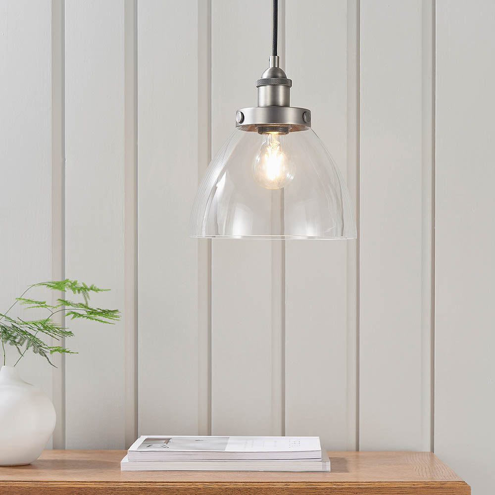 Wentworth Pendant Light in silver with clear dome glass shade and exposed filament bulb, hung above a wooden table in a room with panelled walls.