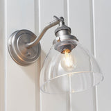Wentworth Wall Light in silver, industrial-style fitting with adjustable knuckle joint, knurled holder and clear glass dome shade, mounted on white wall.
