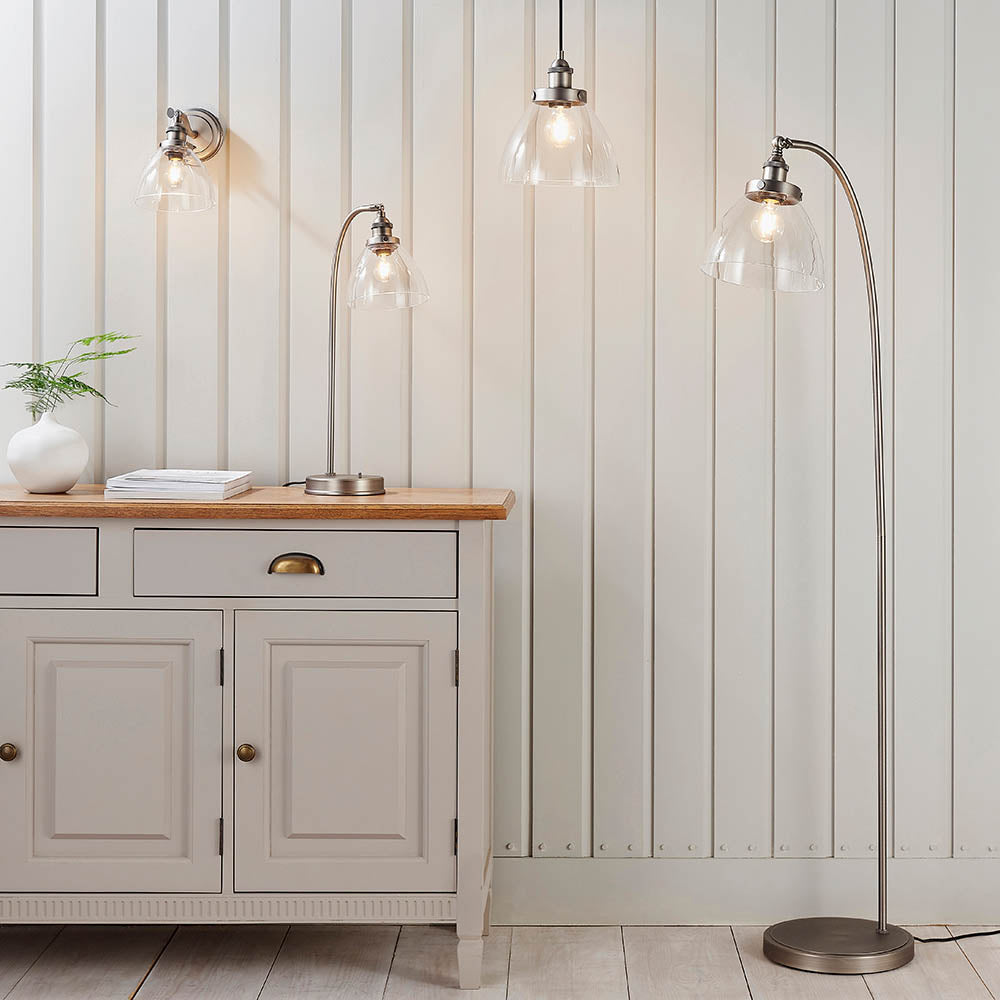 Wentworth Wall Light in silver, industrial-style adjustable fixture with clear glass shade and knurled holder, shown lit on a panelled wall above a sideboard.