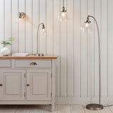 Wentworth Wall Light in silver, industrial-style adjustable fixture with clear glass shade and knurled holder, shown lit on a panelled wall above a sideboard.