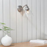Wentworth Wall Light in silver with adjustable knuckle arm and clear glass dome shade, mounted on white panelled wall above a wooden shelf.