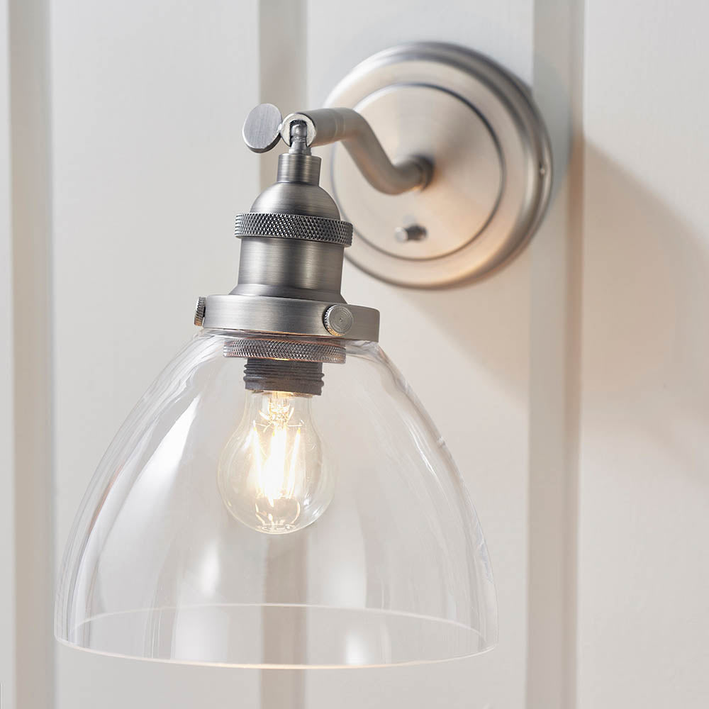 Wentworth Wall Light in silver with adjustable knuckle arm, knurled lamp holder and clear dome glass shade, mounted on a panelled white wall.