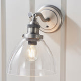 Wentworth Wall Light in silver with adjustable knuckle arm, knurled lamp holder and clear dome glass shade, mounted on a panelled white wall.