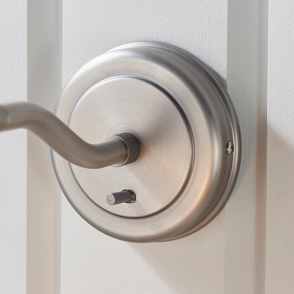 Wentworth Wall Light in silver, close-up of the round base plate and adjustable arm with knurled details, mounted on a white panelled wall.