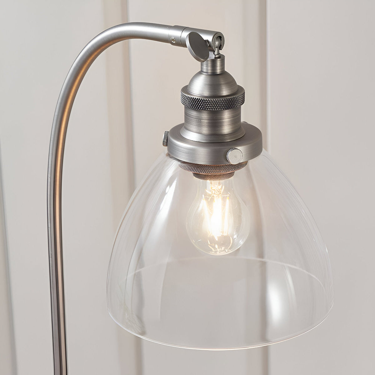 Close-up of the Endon Wentworth table lamp's clear glass dome shade, brushed silver arm, knurled lamp holder, adjustable knuckle and lit E14 filament bulb.