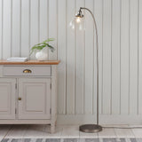 Endon Wentworth arc floor lamp in brushed silver with clear glass shade and E27 filament bulb, beside a grey sideboard in a panelled living room.