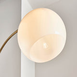 Close-up of Sinclair Floor Lamp's round gloss white glass shade with concave center revealing bulb, on an antique brass curved arm.