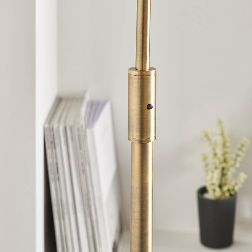Close-up of the Sinclair Floor Lamp's brushed brass stem with a small black on/off switch, shown beside books and a potted plant.