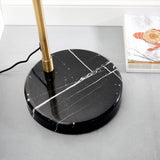 Sinclair Floor Lamp base close-up showing black marble with white veining and a brass stem, set on a grey surface near a magazine.