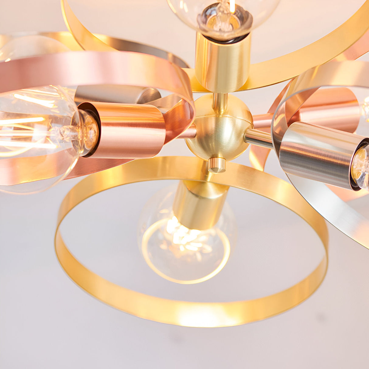 Close-up of the Endon Brenmere 6 light pendant showing its brushed brass central hub with copper, nickel and brass hoops and exposed E27 filament bulbs.