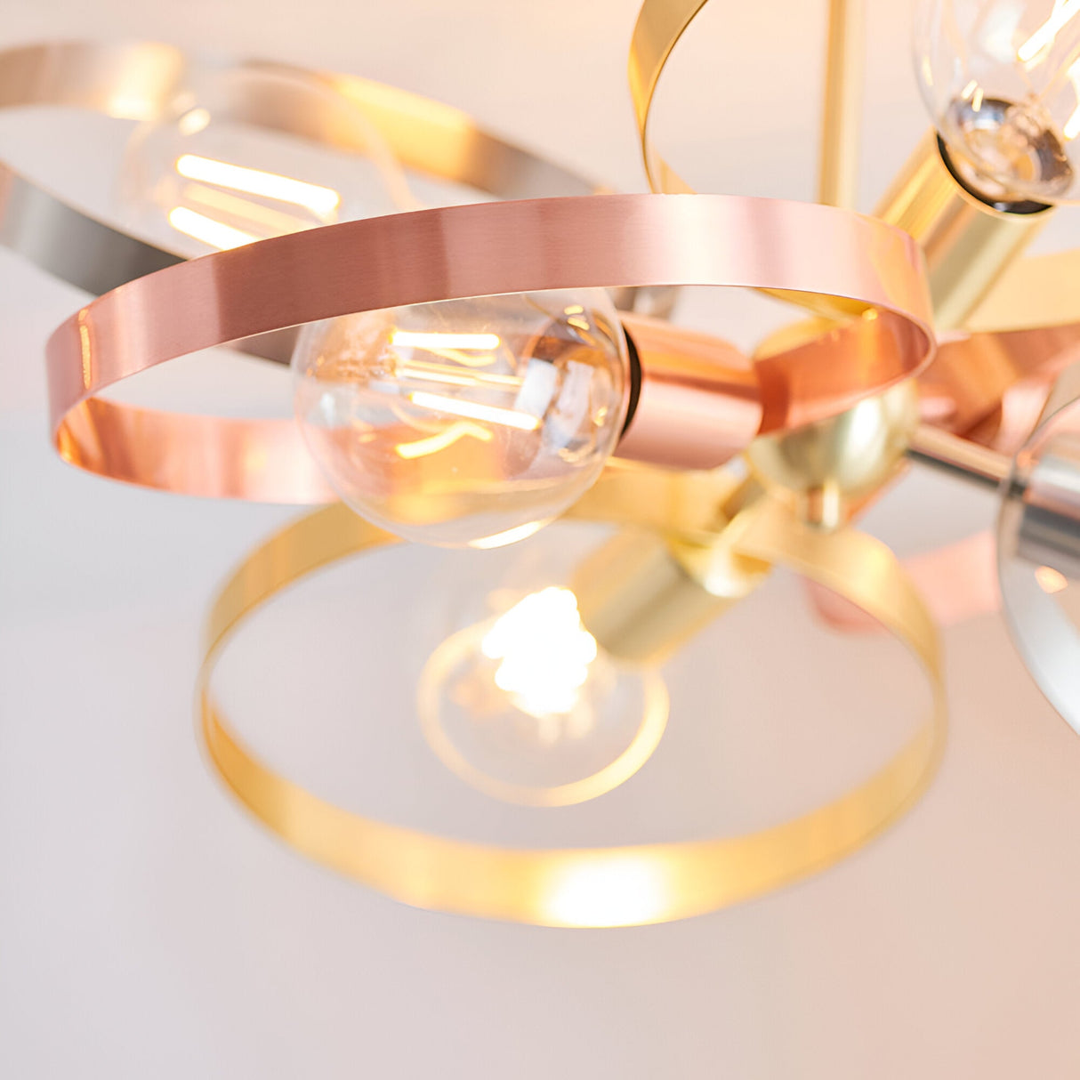 Close-up of the Endon Brenmere 6 light pendant showing brushed copper, brass and nickel open hoops with exposed E27 filament bulbs lit.
