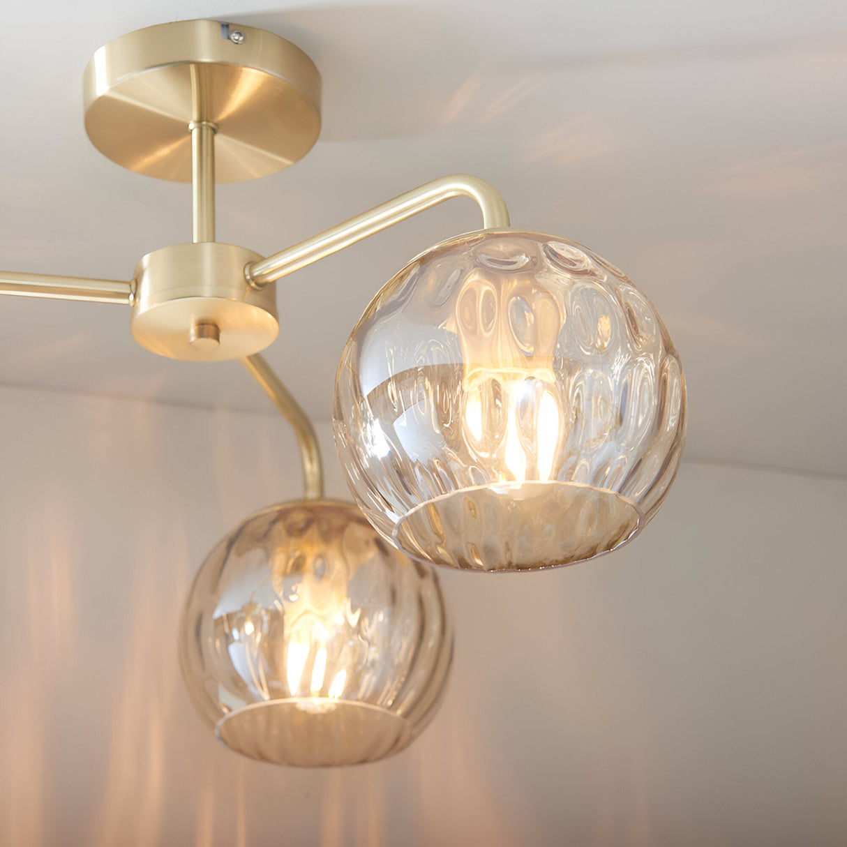 Endon Everly 3 light semi-flush ceiling light in gold, with dimpled glass globe shades on curved brass arms mounted to a circular ceiling plate.