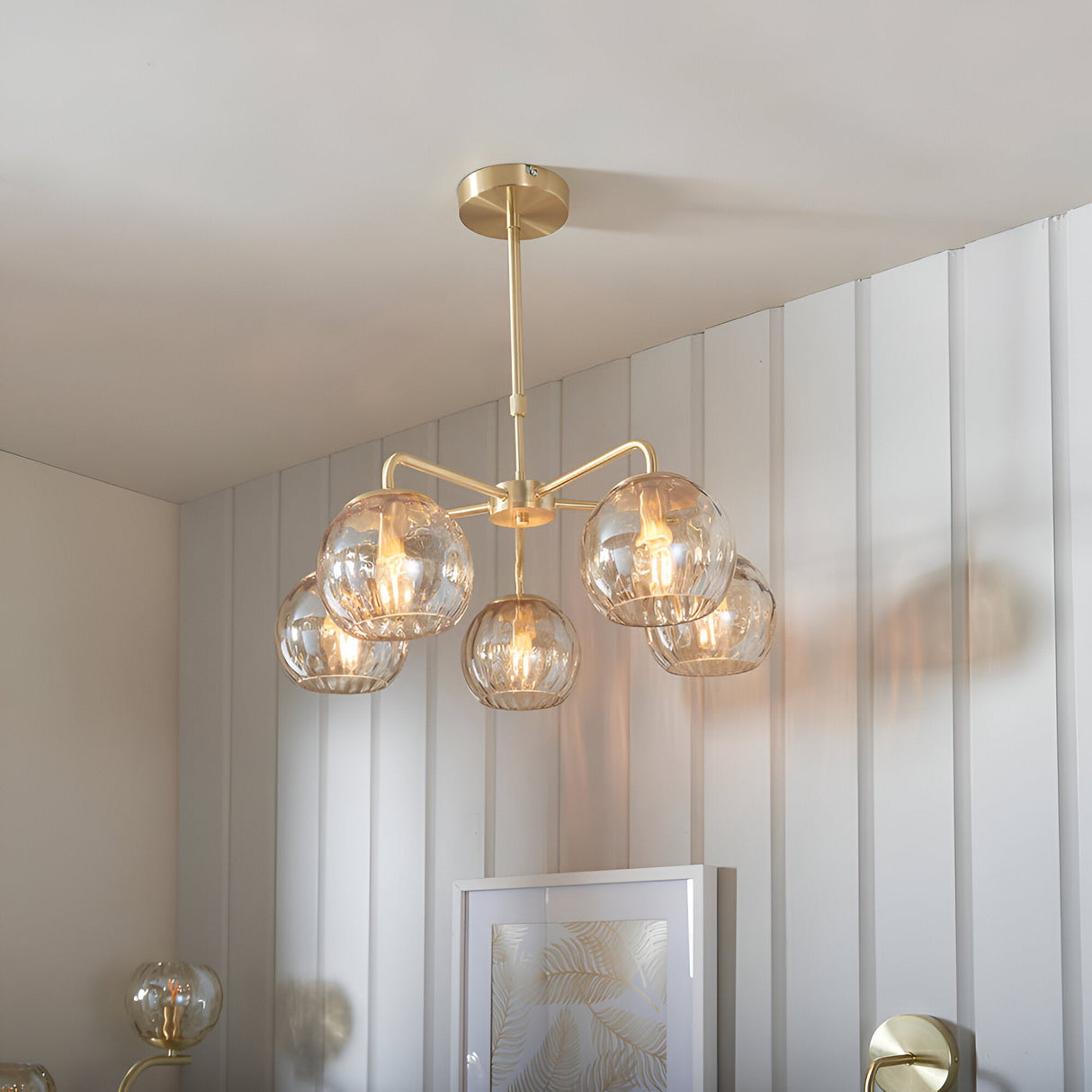Endon Draycott 5 light pendant with champagne dimpled glass globes on a satin brass frame, installed above a framed print in a modern room.