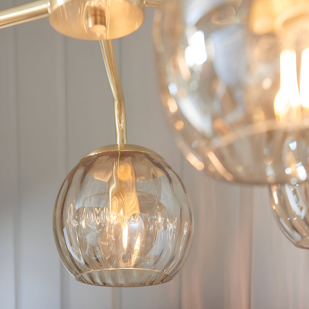 Close-up of Endon Draycott pendant light showing dimpled champagne lustre glass globe shades on satin brass arms against a pale panelled wall.