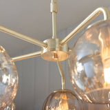 Close-up of the Endon Draycott 5 light pendant showing the satin brass ceiling plate, radiating arms and champagne dimpled glass shades.