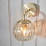 Endon Draycott wall light with a champagne lustre dimpled glass globe shade on a satin brass arm and round backplate, mounted on a white panelled wall.