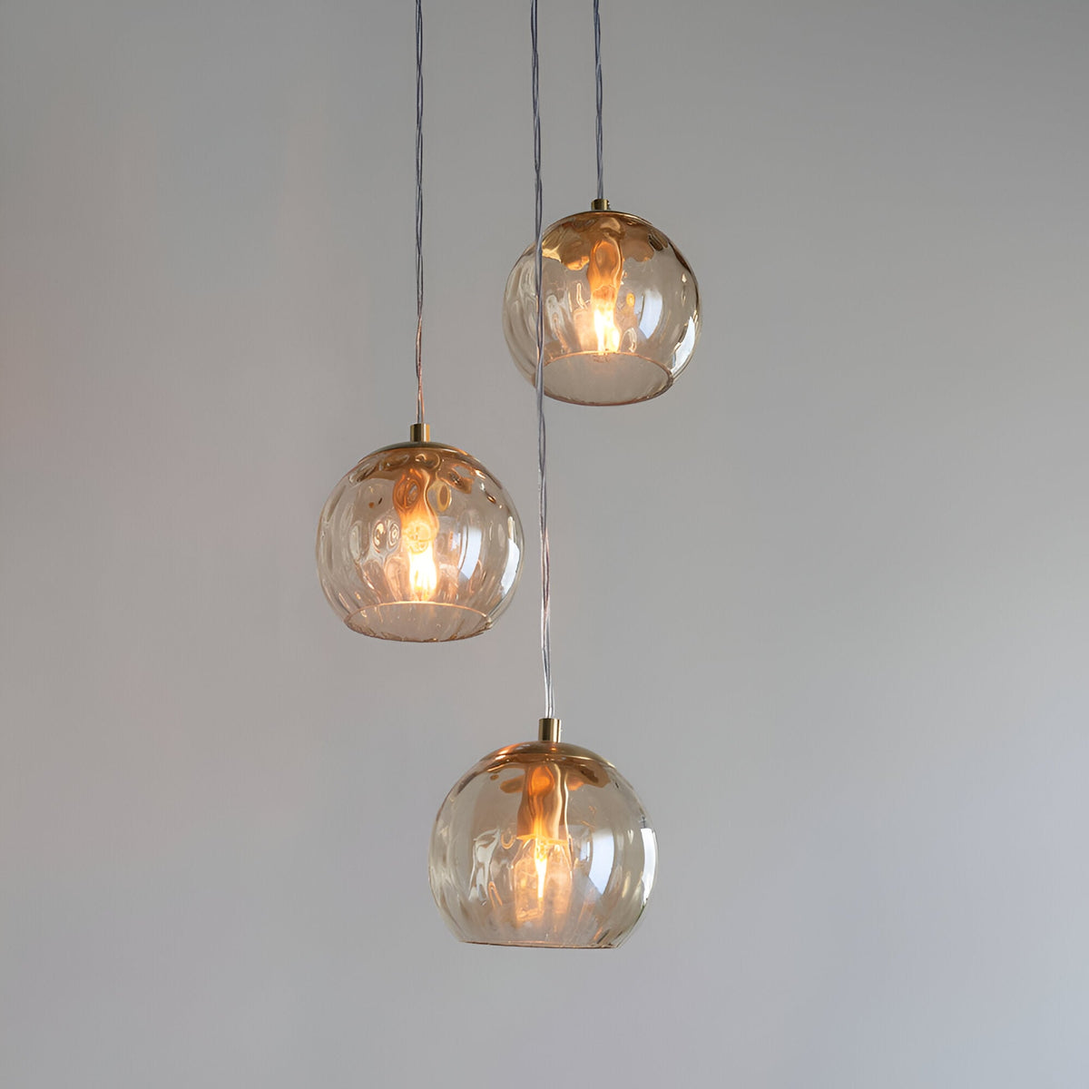Draycott 3-light pendant with dimpled glass globe shades and satin brass fittings, hung at staggered heights on clear cables.