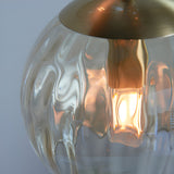 Close-up of the Draycott 3 Light Dimpled Glass Pendant in Satin Brass, showing a textured glass shade with a lit bulb beneath the brushed brass canopy.