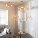 Draycott Dimpled Glass Table Lamp in satin gold on a round side table, shown alongside matching pendant, floor and wall lights in a living room setting.