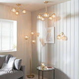 Endon Draycott 3-light floor lamp with champagne dimpled glass shades on a satin brass stem, shown in a living room corner beside a grey sofa.