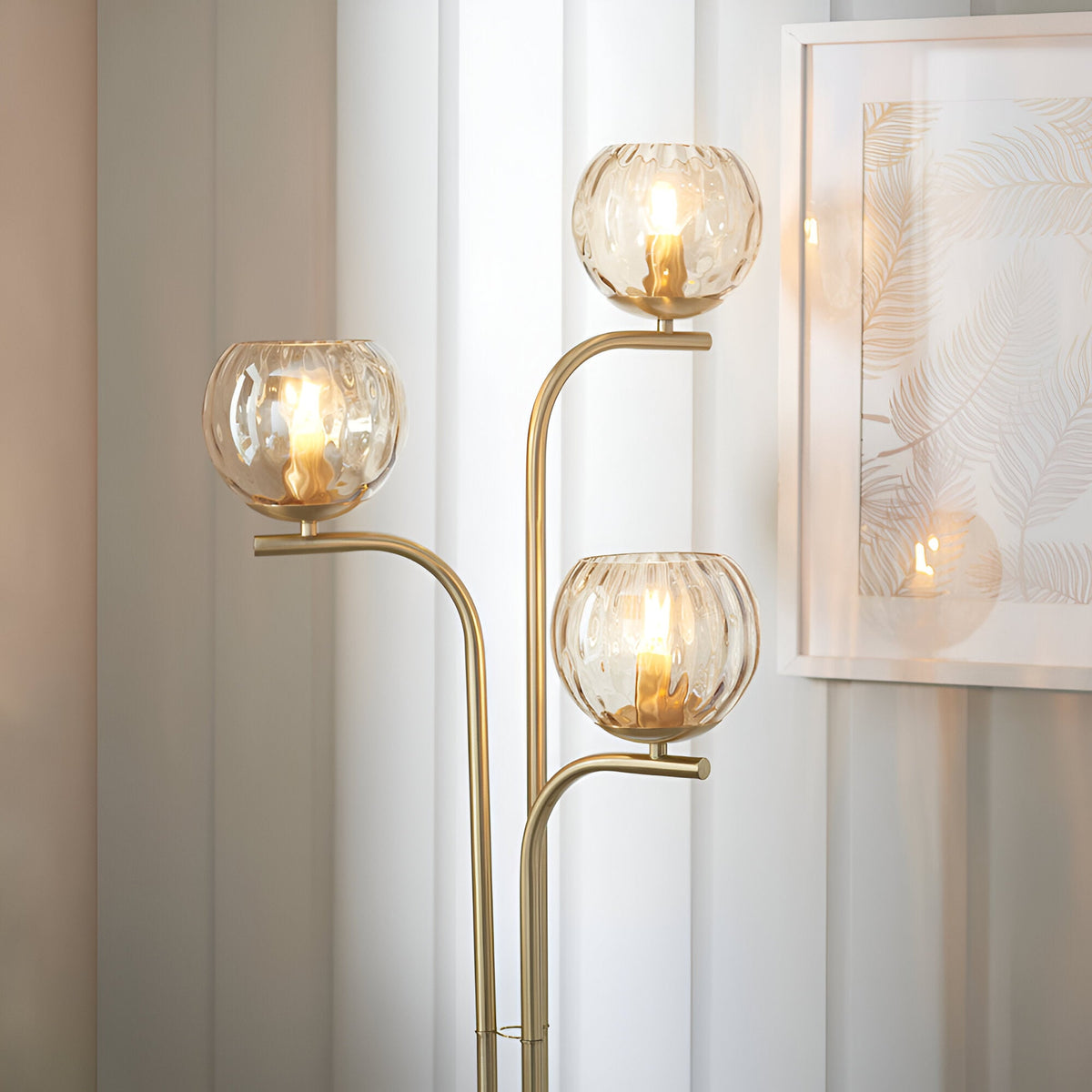 Endon Draycott 3 light floor lamp with champagne dimpled glass globe shades on a satin brass stem, styled beside sheer curtains and a framed print.