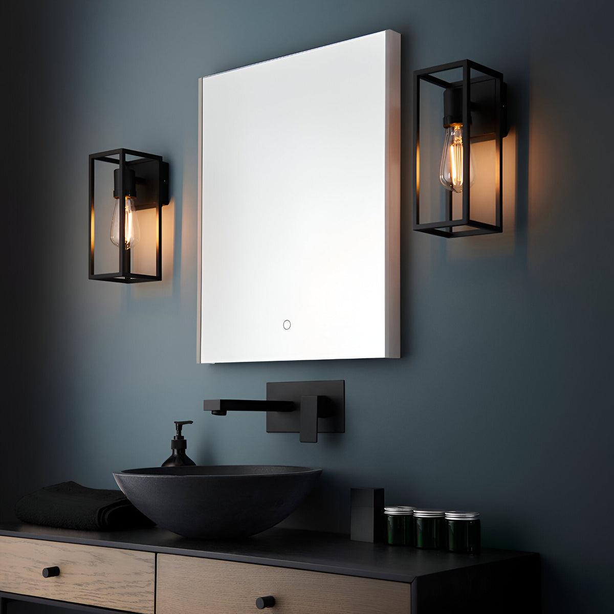 Brenford Outdoor Wall Light in black, cage-style aluminium frame with exposed filament bulb, shown either side of a bathroom mirror above a dark vessel sink.