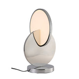 The Half Moon LED Table Lamp - Silver features a modern oval light partially encased in a shiny chrome-finished curved plate, with a circular metallic base and body, minimalist design, and black power cord extending from the base.