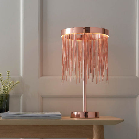 Endon Danestead LED table lamp in brushed copper with cascading fine chains from a ring shade, styled on a wooden console against a panelled wall.