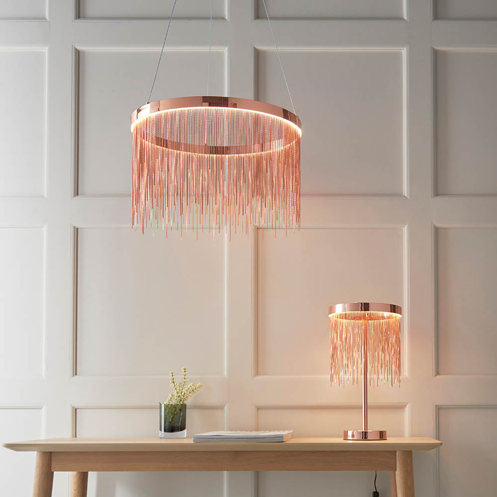 Endon Danestead table lamp in brushed copper with fine chain fringe under an LED ring, shown on a wooden console beside a matching pendant.