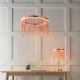 Endon Danestead table lamp in brushed copper with fine chain fringe under an LED ring, shown on a wooden console beside a matching pendant.