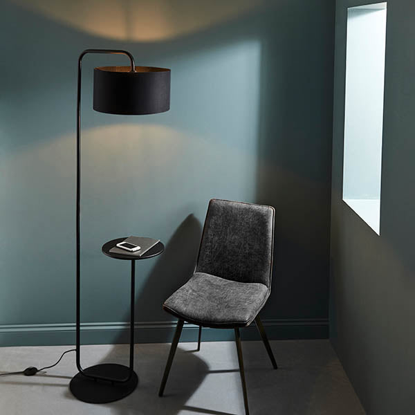 Caldfield Floor Lamp in satin black metal with a cylinder fabric shade and built-in round table top, shown beside a grey chair in a living room setting.