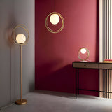 Endon Brackshaw brushed gold floor lamp with opal glass orb in three interlinking rings, shown with matching pendant and table lamps against a burgundy wall.