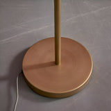Close-up of the Endon Brackshaw floor lamp's round brushed gold base and stem with grey fabric cable on a scratched grey surface.