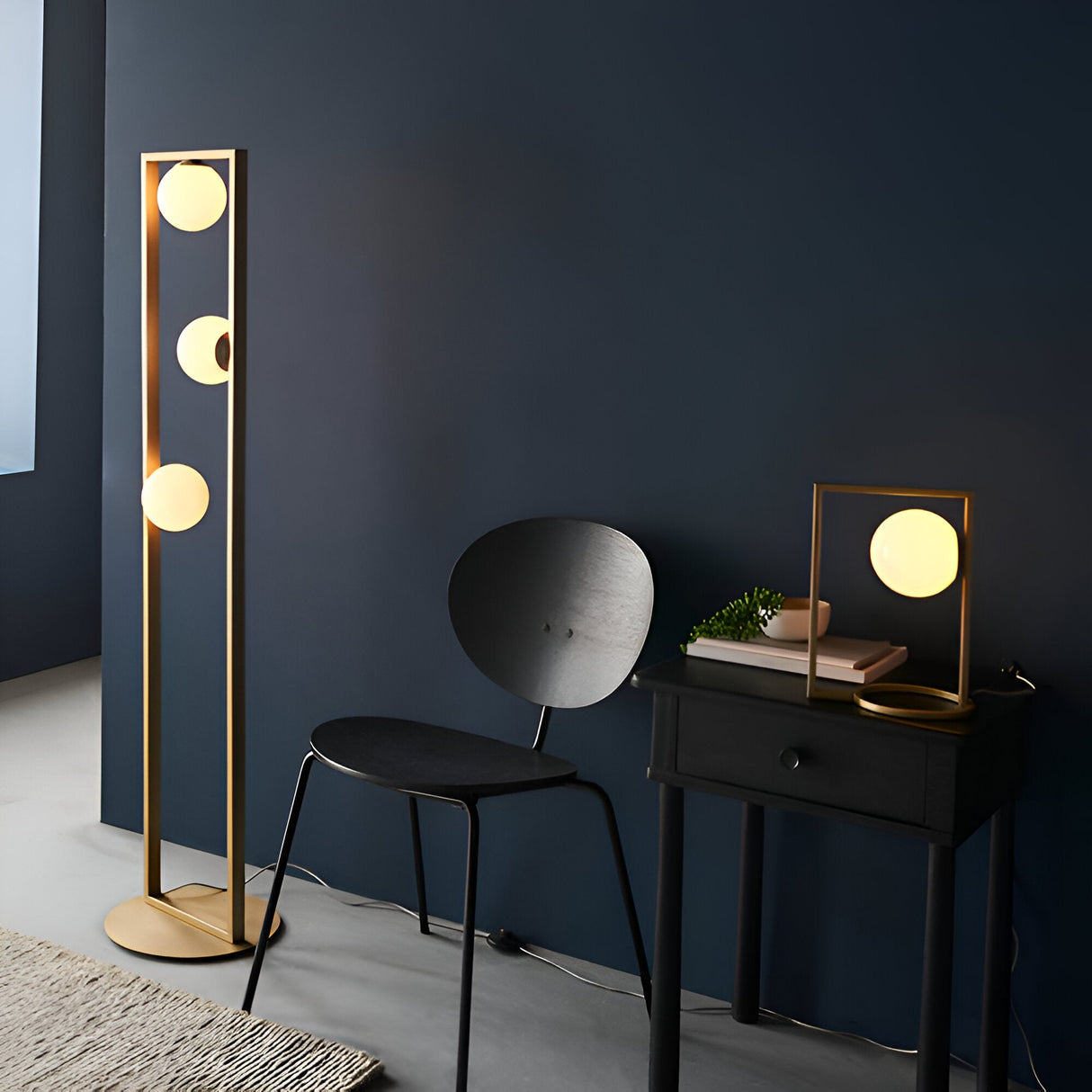 Cranford 3 Light Floor Lamp in brushed gold with opal glass spheres on an angular frame, shown beside a black chair and side table.