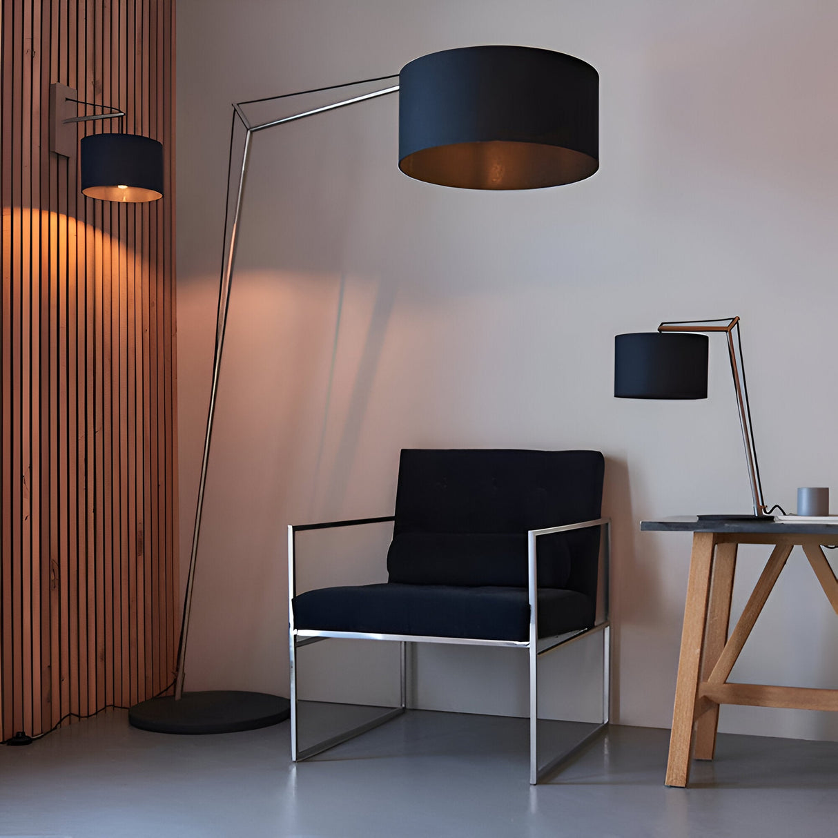 Carlfield Floor Lamp in nickel with black cotton drum shade on a cantilevered arm, shown beside a black armchair in a living room setting.